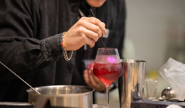 Close-up of a professional bartender stirring a red cocktail