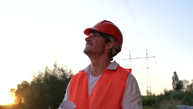 Smiling electrical engineer holding the drawing and looking at the power transmission. Highest voltage transmission. Energy industry concept. Slow motion