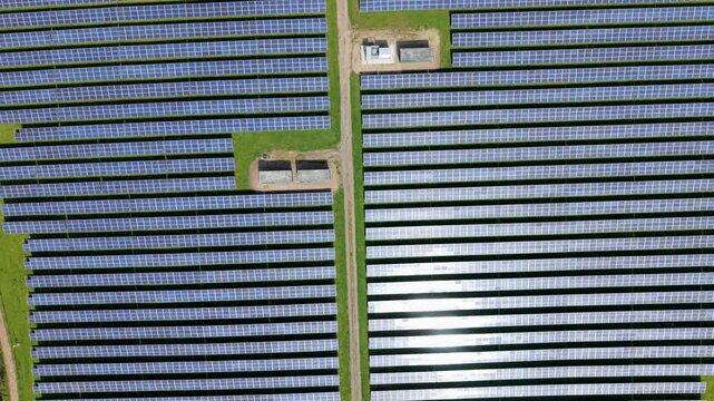 Aerial view of a utility-scale solar farm with symmetrical rows of cells, showcasing advanced renewable energy infrastructure and transformer units in Tutbury, UK.