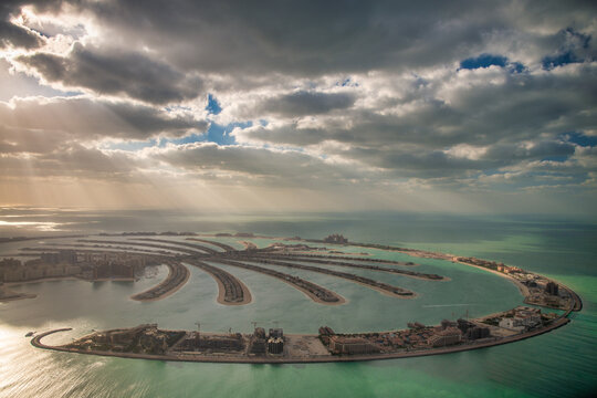 Breathtaking aerial view of Palm Jumeirah Dubai at sunset with sunlight filtering through dramatic clouds