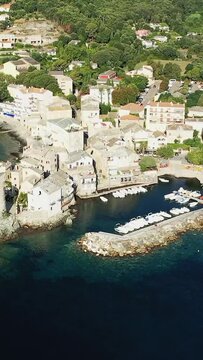 Scenic aerial shot of Erbalunga village and its picturesque harbor with boats docked along the coastline, surrounded by lush greenery in Corsica, France.