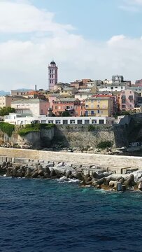 Scenic view of Bastia's colorful historic buildings and waterfront along the Mediterranean Sea in Corsica, France, under a partly cloudy sky.