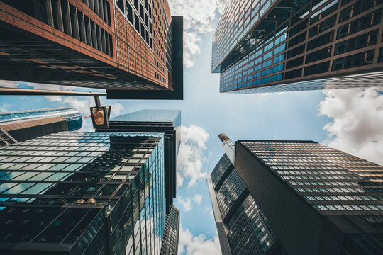 View of towering skyscrapers reaching for the sky, their glass facades reflecting the scattered clouds and sunlight in Frankfurt am Main, Hessen, Germany.