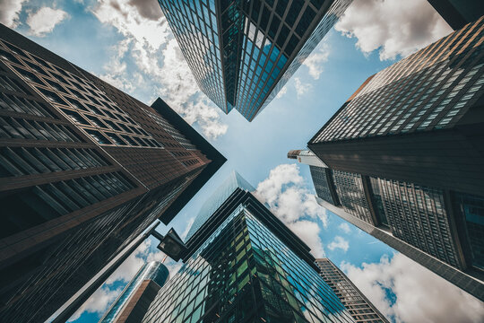View of towering skyscrapers reaching up to a vibrant blue sky dotted with fluffy white clouds, creating a dynamic contrast of glass and sky, Frankfurt, Hessen, Germany.