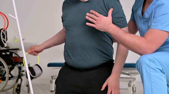 Adult patient with disability performing strength exercises using light weights assisted by physiotherapist. Rehabilitation, mobility improvement, motor skills and recovery in healthcare clinic. 