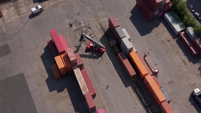 Drone aerial of a freight terminal near Milan, Italy. Reach stackers and yard tractors actively loading and repositioning shipping containers in a high-intensity logistics environment.