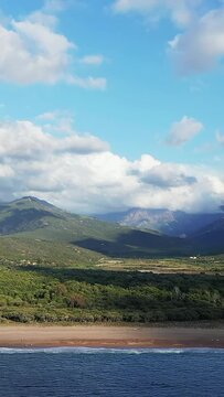 Scenic view of the Delta du Fango with lush greenery, sandy beach, and dramatic mountains under a partly cloudy sky in Corsica, France.