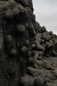 View of dark, porous lava rock formations rise from the barren landscape under an overcast sky, contrasting textures in Skaftarhreppur, Skaftarhreppur, Iceland.