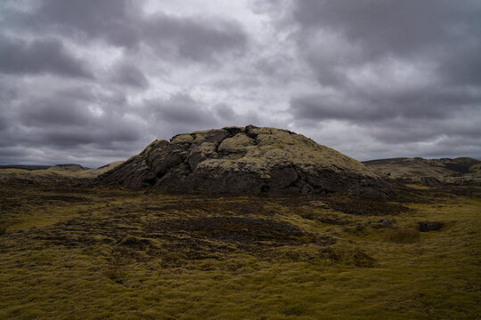 View of a moss-covered hill under a cloudy sky, standing stark against the textured landscape, creating a scene of Icelandic beauty, Skaftarhreppur, Iceland.