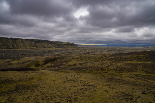 View of a vast, rugged landscape with moss-covered lava fields stretching under a dramatic, brooding sky, Skaftarhreppur, Iceland.