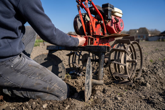 Person installing hiller attachment on walk behind tractor, agricultural implement used for forming soil ridges during field cultivation.