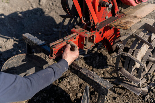 Person installing hiller attachment on walk behind tractor, agricultural implement used for forming soil ridges during field cultivation.