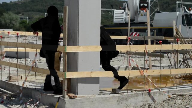 Team of construction laborers executing manual work and operating machinery at busy urban building project site