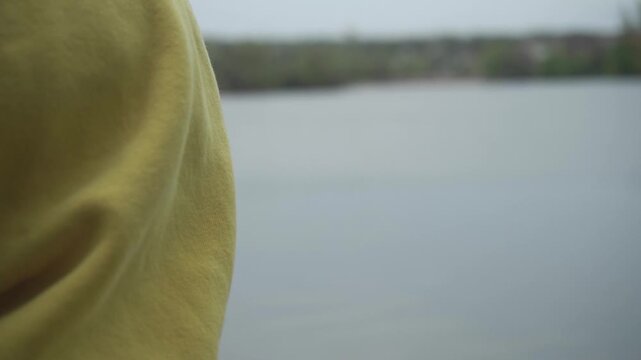 A solitary figure, dressed in a contemplative yellow hooded garment, stands by a serene water surface, inviting calm