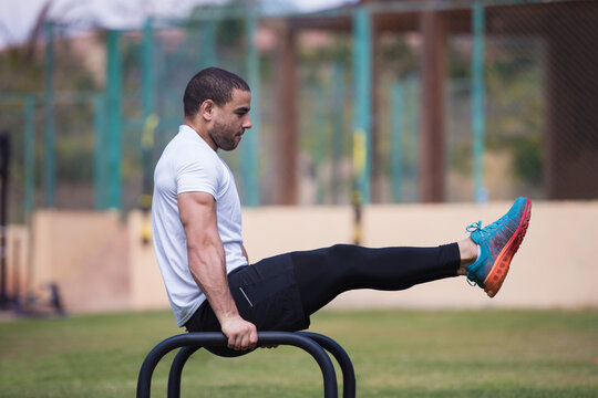 Man doing L-sit calisthenics on parallel bars during outdoor crossfit fitness workout with a friend