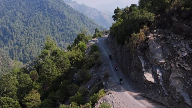Aerial view of motorcyclists riding on a narrow rocky mountain road with sharp bends and steep cliffs. Adventure touring, remote travel, and rugged nature landscape captured in daylight.
