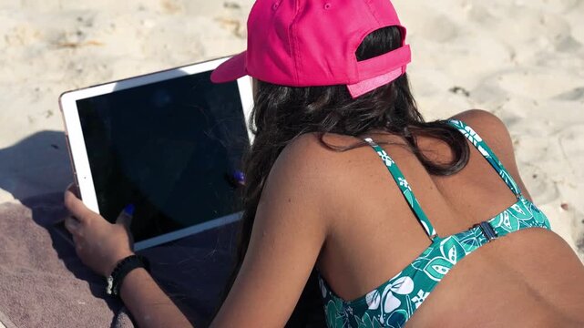 Female traveler reclining on the shore enjoying digital device and seaside view