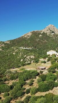 Scenic mountain view with lush greenery and rustic houses under a clear blue sky in Pigna, Corsica. Tranquil Mediterranean countryside setting.