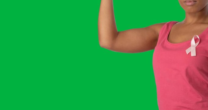 Mid section of woman wearing pink top with ribbon badge flexing her biceps against black background