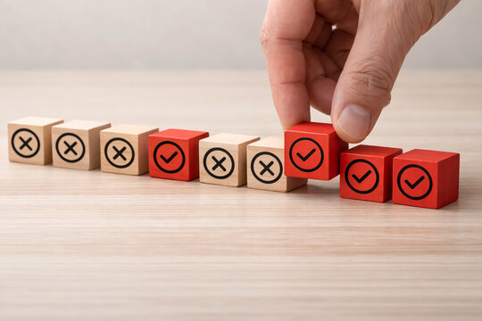 Hand places a red wooden cube with a checkmark onto a line of blocks showing both cross marks and check symbols to illustrate the process of identifying and correcting errors.
