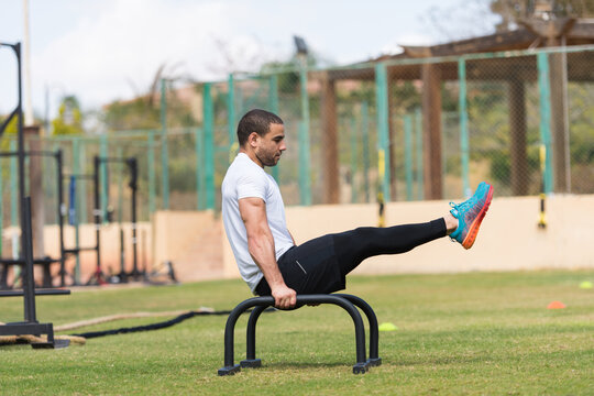 Athletic man performing L-sit on parallel bars during outdoor CrossFit workout session