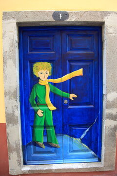 A beautiful color street art mural of The Little Prince painted on a bright blue door in Funchal, Madeira, Portugal