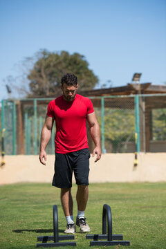 Man doing outdoor CrossFit workout using parallel bars in a sunny park training session with friend