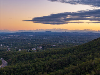 Fototapeta premium Breathtaking twilight panorama of Brisbane city, its sprawling suburbs, and distant mountains under a radiant sunset sky.