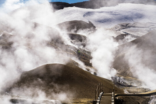 View of geothermal steam rises from the earth against a stark backdrop of snow-capped mountains, creating a surreal landscape of contrasting elements, Hrunamannahreppur, Iceland.
