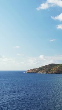 Wide view of the blue sea and rugged coastline under a clear sky at Delta du Fango, Corsica. Tranquil Mediterranean scenery with distant hills and calm water.