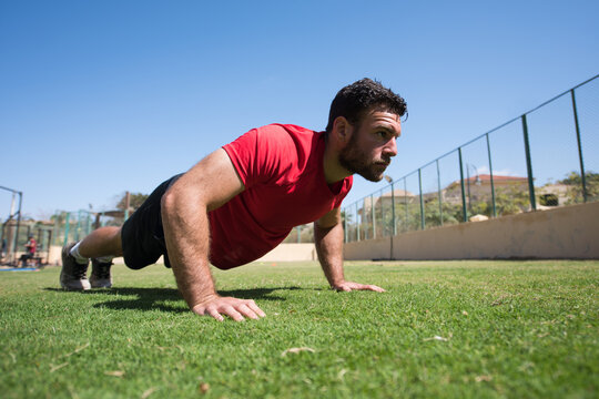 Man doing push-ups outdoors at a CrossFit style open-air fitness gym with focused expression