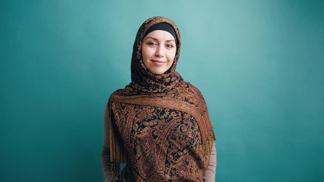 Confident Muslim woman wearing a traditional patterned hijab looking and smiling at the camera against a solid background