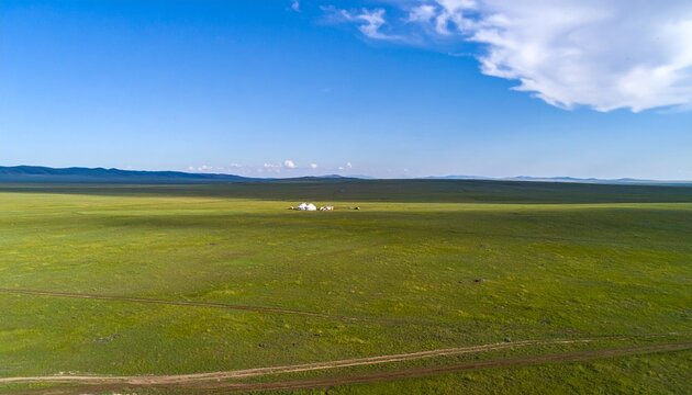 Aerial view of Mongolian steppe with distant ger camp under clear blue sky