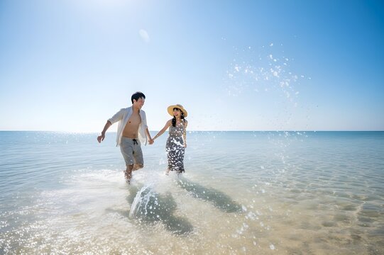 夏の海で遊びながら楽しい時間を過ごす日本人カップルの爽やかなビーチ風景（AI生成）