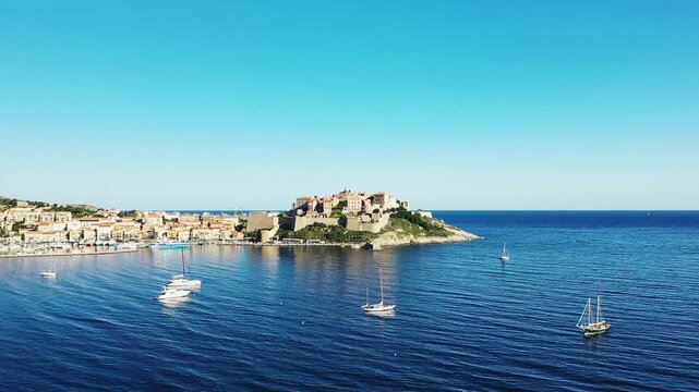 Scenic view of Calvi citadel and harbor with sailboats on the blue Mediterranean Sea under a clear sky in Corsica, France.
