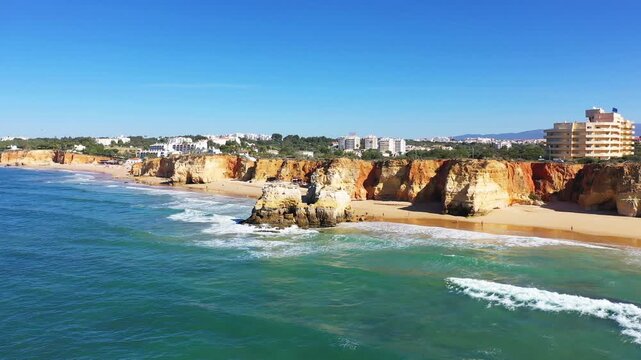 Scenic view of Algarve s dramatic cliffs and sandy beach with turquoise waves and clear blue sky, near Albufeira, Portugal.