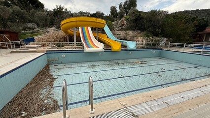 Abandoned outdoor swimming pool with empty water slides and overgrown surroundings © dvoevnore