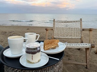 Outdoor seaside breakfast with coffee, dessert, and empty chair on a sandy beach at sunrise © dvoevnore