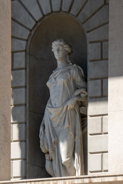 A standing marble statue of a draped female figure within a rusticated stone niche.

