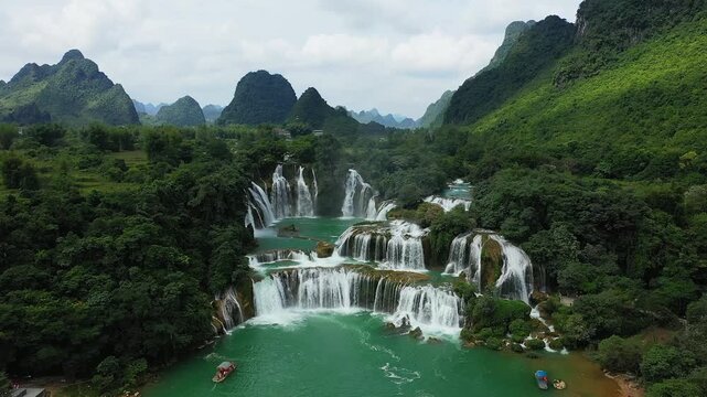 Aerial view of Ban Gioc Waterfall cascading through vibrant green forest and dramatic limestone mountains in northern Vietnam. Turquoise river and scenic landscape create a breathtaking natural scene.