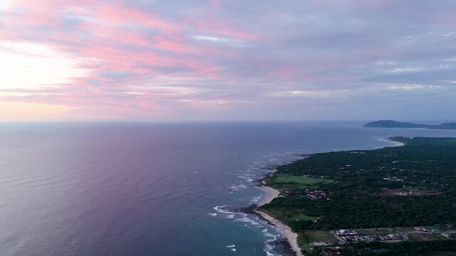 Stunning aerial perspective of the lush costa rican coastline at avellanas beach. The pacific ocean meets a sandy shore and dense forest under a sky painted with vibrant pink and purple sunset clouds