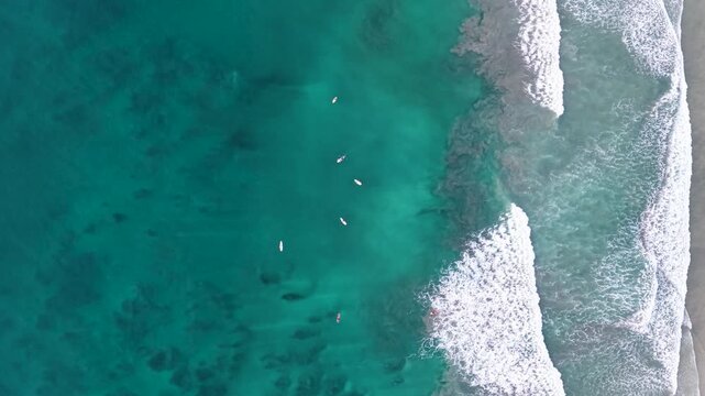 Majestic aerial top-down view of surfers in the emerald green ocean at avellanas beach, costa rica. People waiting to ride the waves