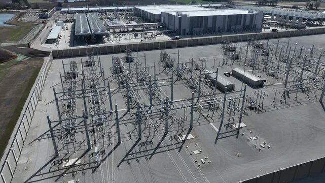 Aerial drone shot panning across high-voltage electrical substation with AI data center in background, showing power infrastructure, grid connectivity, and industrial energy systems.
