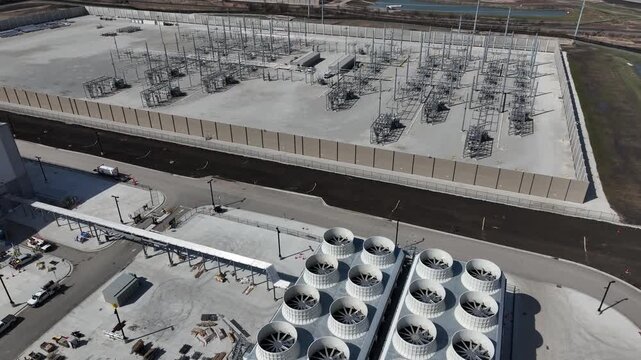 Aerial pan from cooling towers of a data center to a large electrical substation, with another facility under construction in the distance, showcasing power infrastructure for AI and cloud computing.