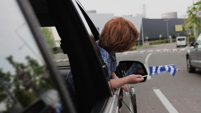 Cute boy holding Greece flag, looking out the window. Slow motion