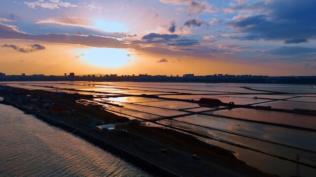 Aerial view of salt evaporation ponds during golden sunset. Sunset reflection in geometric salt pans near city skyline at dusk.