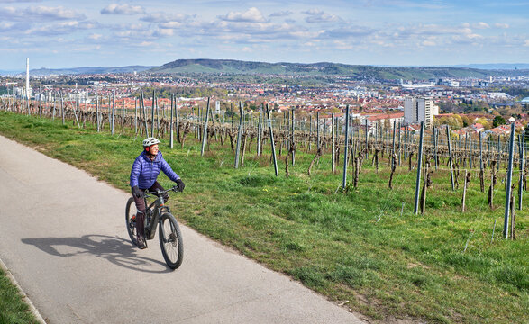 Active senior woman riding an electric mountain bike through vineyards above Stuttgart, Germany. Enjoying spring sunshine with scenic city views, green hills, and a peaceful countryside atmosphere.