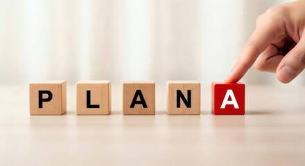 Naklejka premium Business Planning and Strategy Concept. Hand placing red cube with letter A next to wooden blocks forming word PLAN, representing primary plan selection and strategic decision making. 