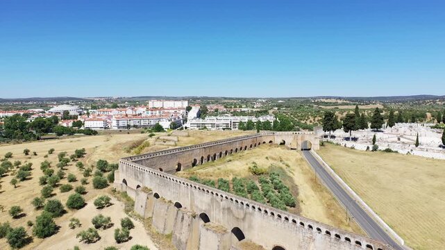 Aerial view of the historic aqueduct stretching across the rural landscape near Elvas, Portugal, with the town visible in the background under a clear blue sky.