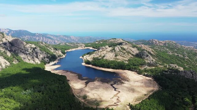 Scenic aerial view of Lac de l Ospedale surrounded by lush green forest and rugged mountains in Corsica, France under a blue sky.